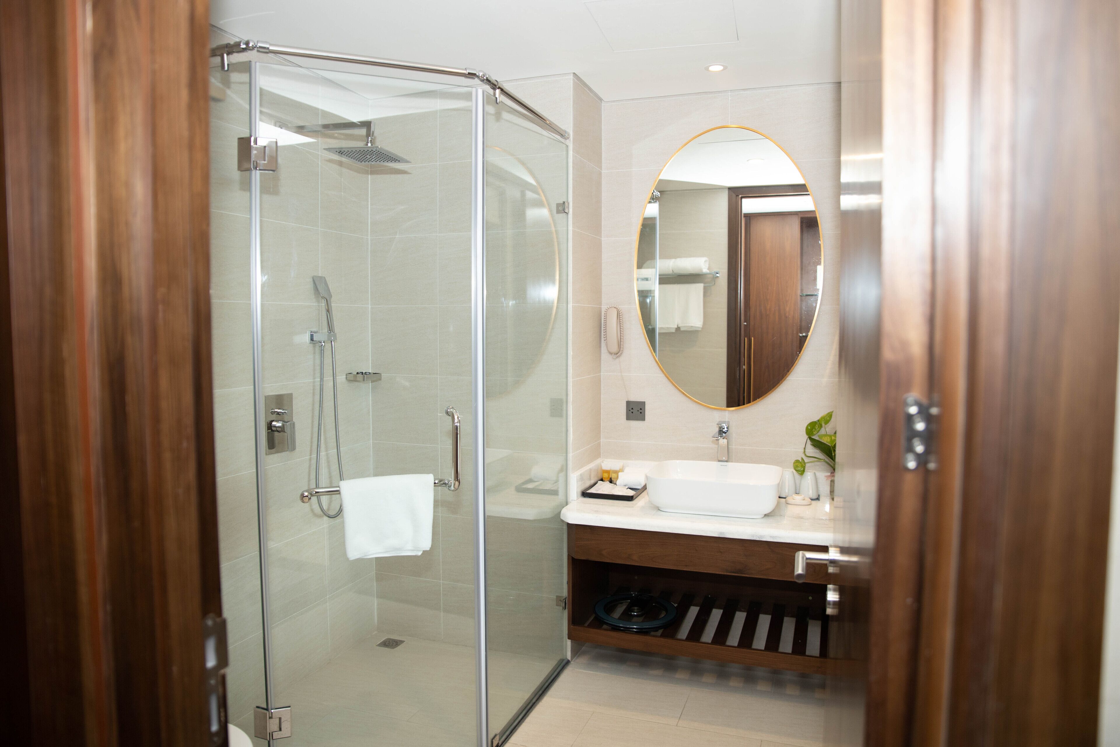 Un baño moderno con ducha de vidrio, tocador de madera y espejo redondo.