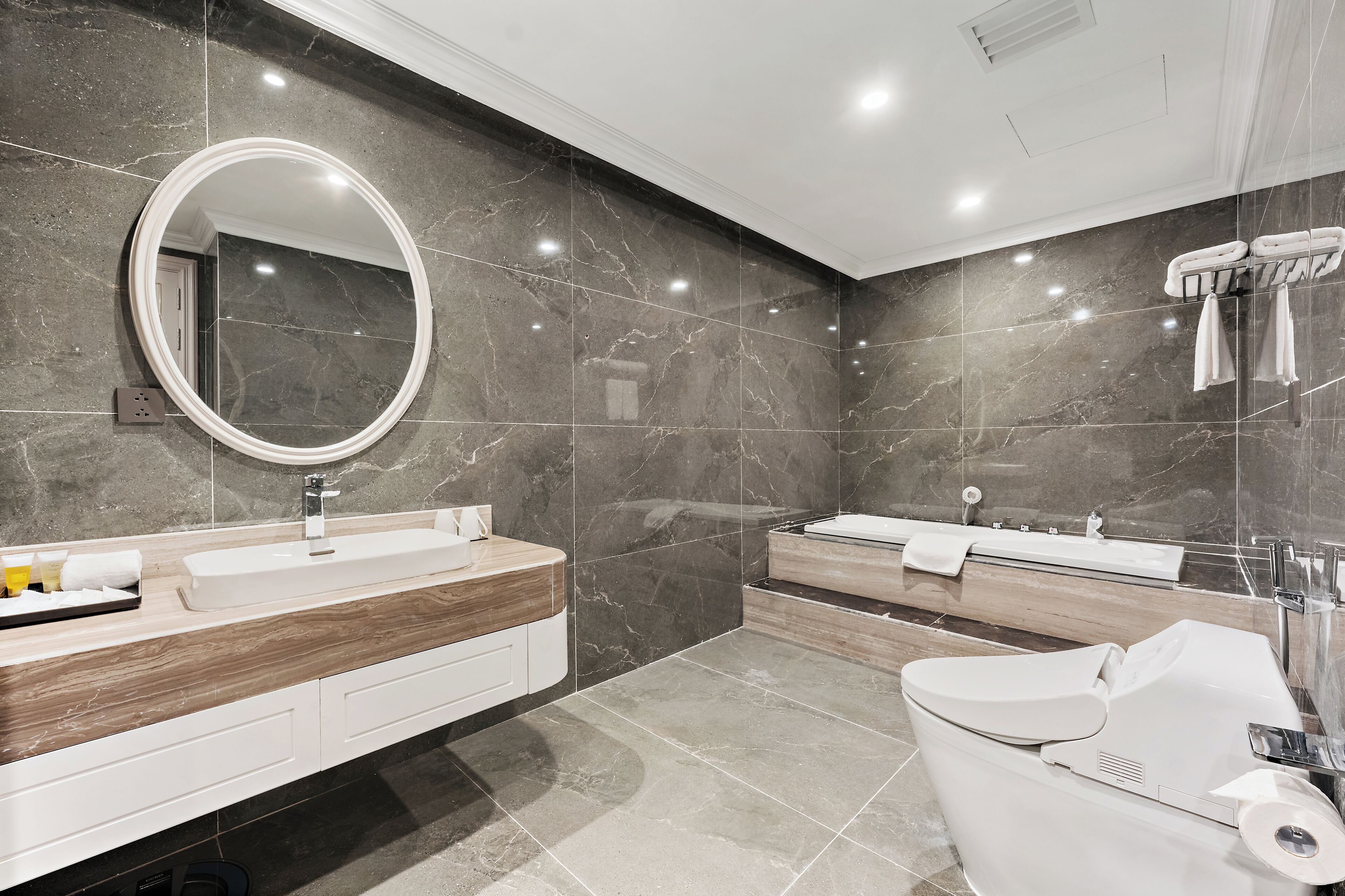 A modern bathroom with a large mirror, two sinks, a bathtub, and a toilet.