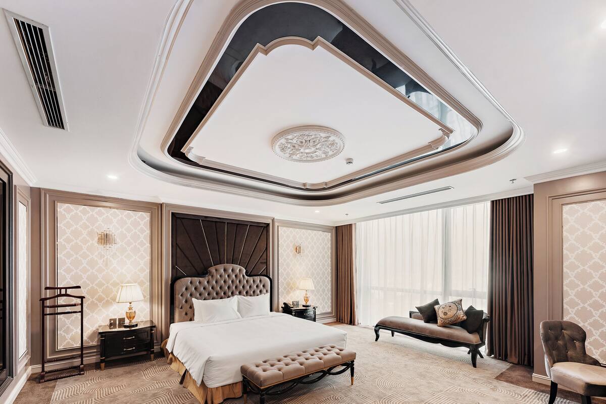 Um quarto luxuoso com uma cama grande, uma mesinha de cabeceira, um banquinho e uma cadeira.