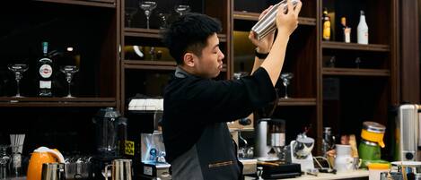 A barista preparing a drink behind a counter with various coffee-making equipment and glassware.