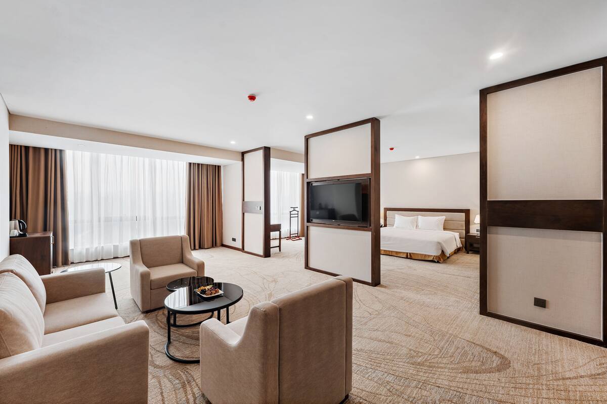 Quarto de hotel com sofá, poltrona, televisão, cama e uma mesinha com uma bandeja de petiscos.