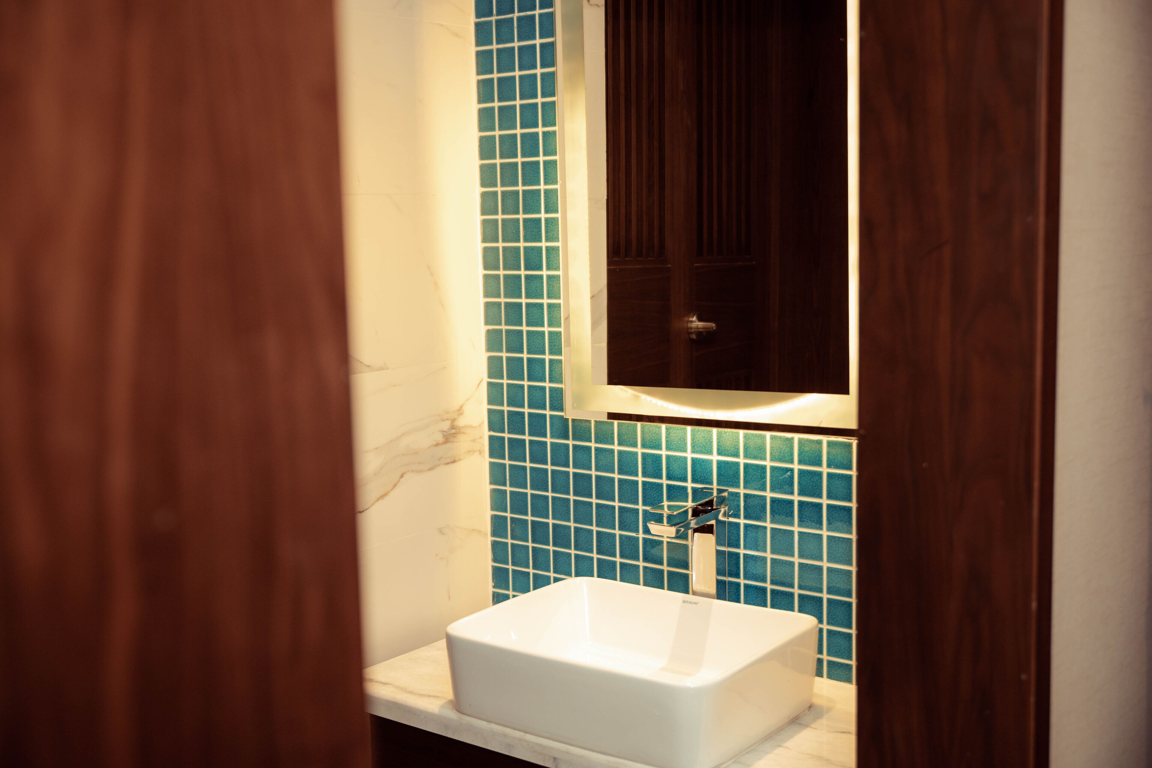 Un baño con un lavamanos blanco, pared de azulejos azules y una puerta de madera.