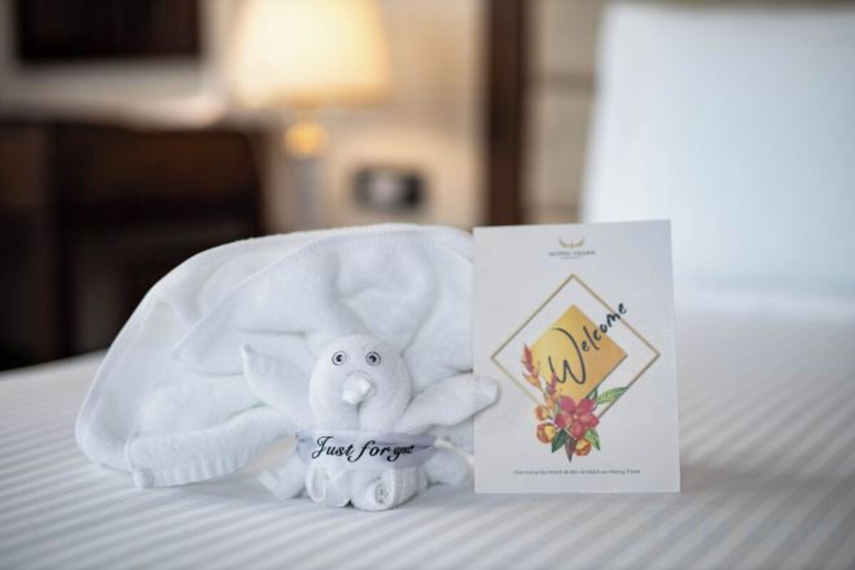 A neatly made bed with a plush toy and a welcome card.