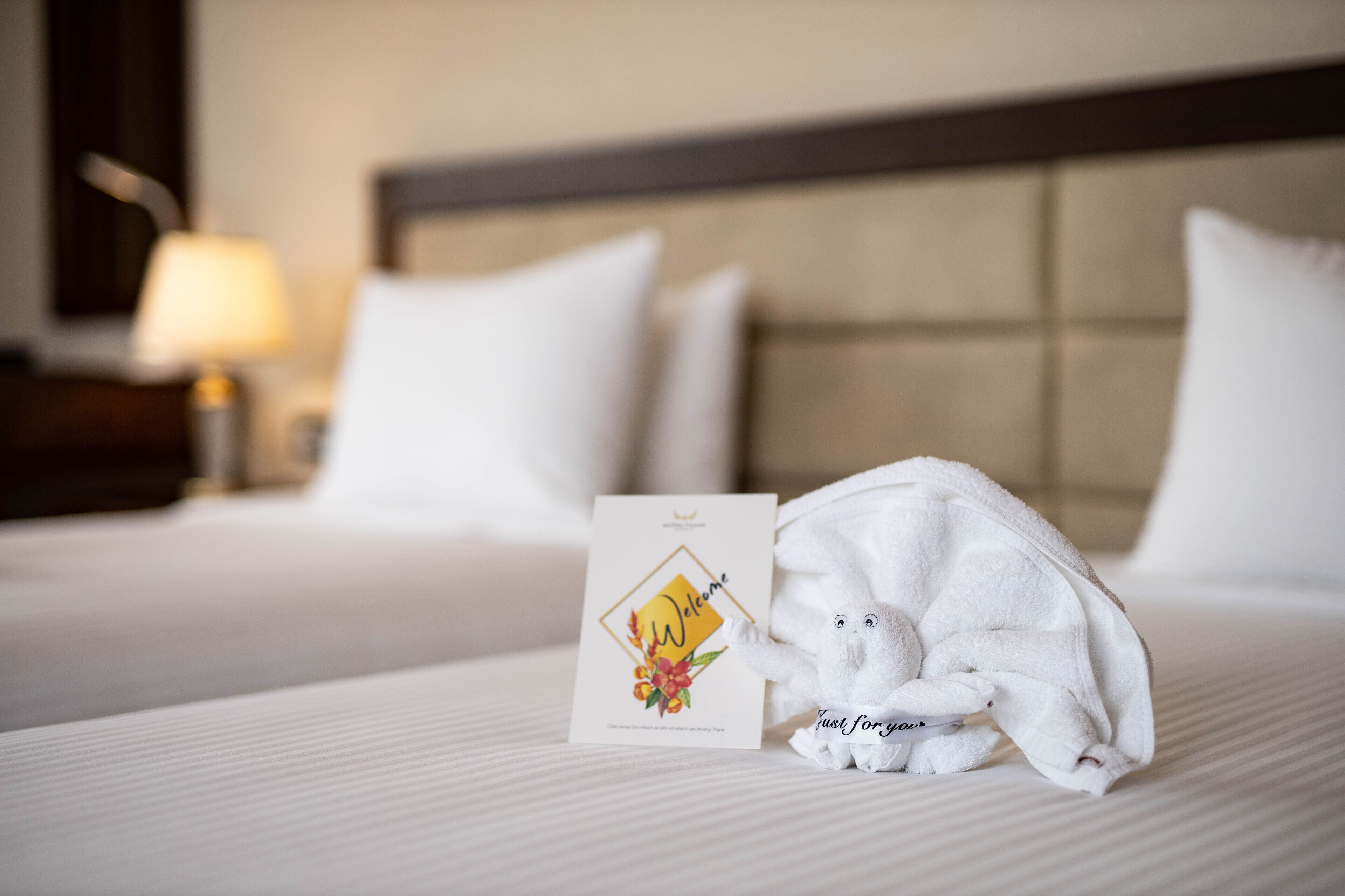 A neatly made bed with a welcome card and a towel shaped like a small animal.