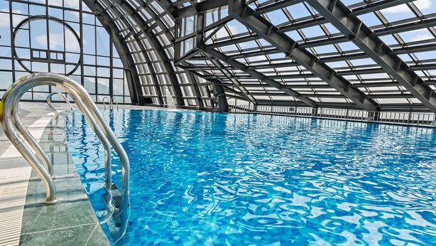 An indoor swimming pool with clear blue water, metal pool ladders, and a modern architectural design with large windows and a curved roof. - Muong Thanh Luxury Cao Bang Hotel (Thuc Phan)