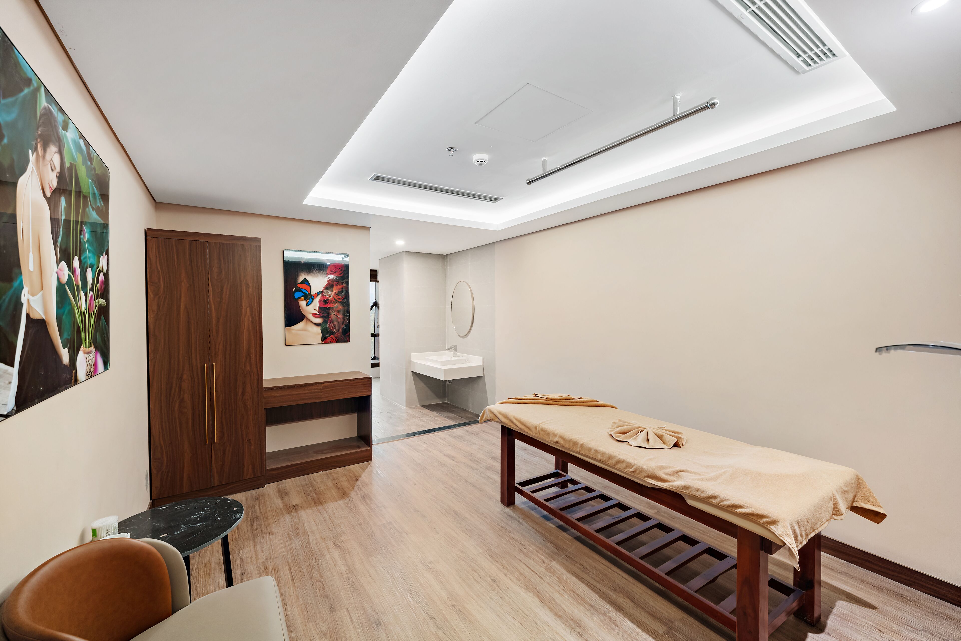 A modern room with a wooden bench, a small table, a chair, a sink, and a large painting on the wall.
