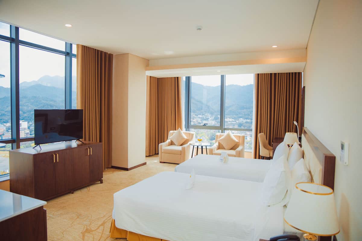 Quarto de hotel com duas camas, televisão, secretária e vista para montanhas.