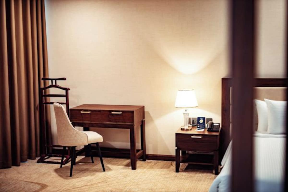 Una habitación de hotel con escritorio, silla, mesita de noche, lámpara y cama.