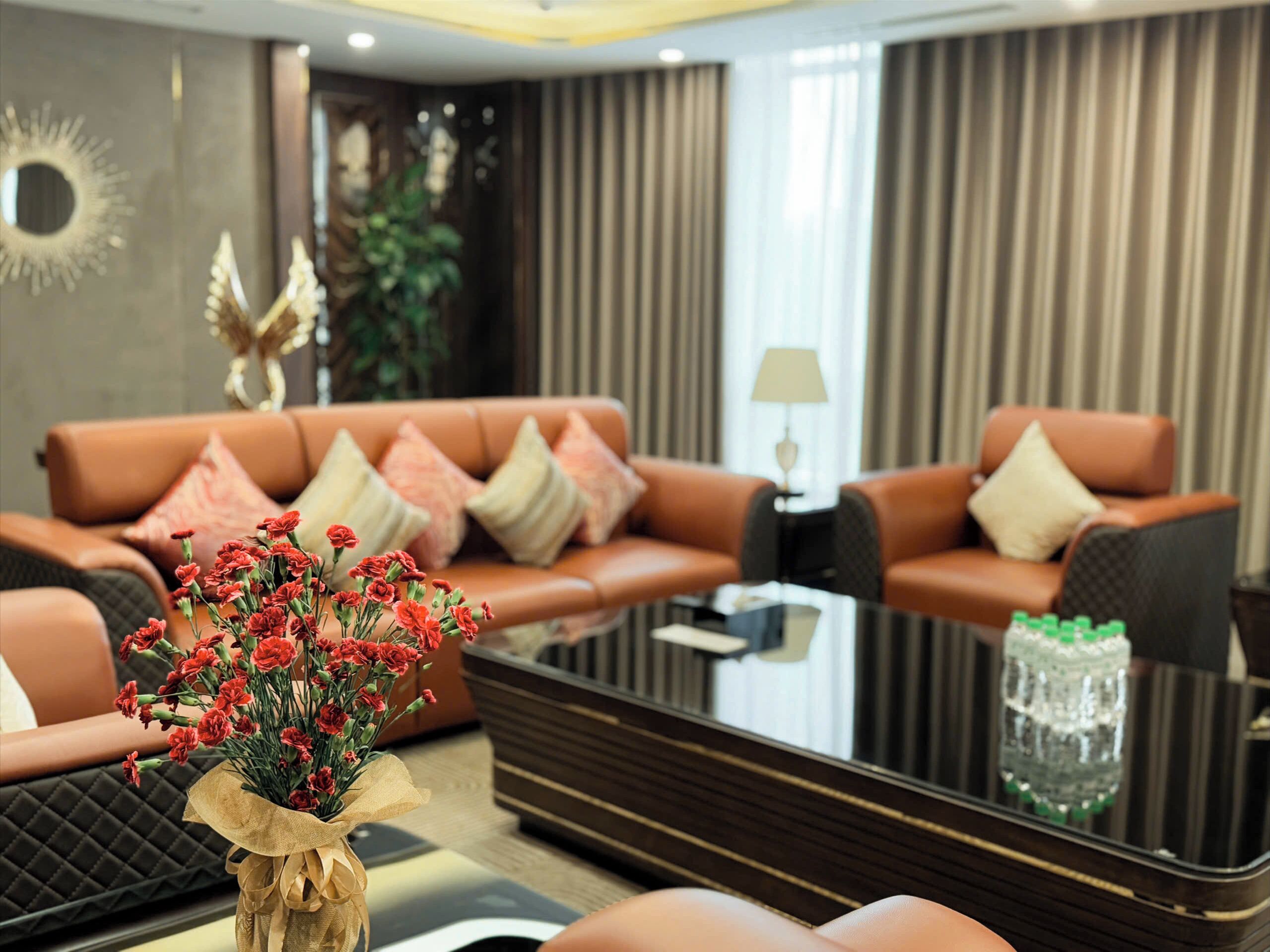 A modern living room with a brown leather sofa, a glass coffee table, and a vase of red flowers.