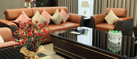 A modern living room with a brown leather sofa, a glass coffee table, and a vase of red flowers.