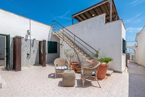 A rooftop patio with wicker furniture, a staircase, and potted plants.