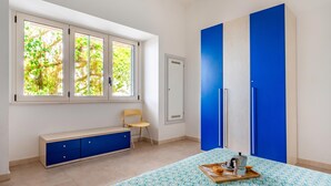 Ein Zimmer mit einem Bett, einem Fenster mit Blick auf Bäume, einem blauen Kleiderschrank, einer Bank und einem Tablett mit einer Kaffeemaschine.