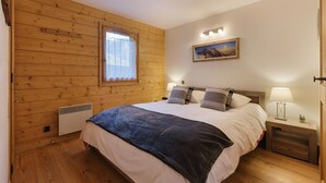 A bedroom with a wooden wall, a bed with a dark blanket, two bedside lamps, a nightstand, and a painting on the wall. - Appt Bec A2 Alpine retreat & ski at Mont Blanc Valley, Le Tour (Argentière), France (Le Tour (Argentière))