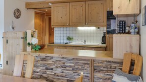 A kitchen with wooden cabinets, a stone backsplash, and a dining area with a table and chairs. - Appt Bec A2 Alpine retreat & ski at Mont Blanc Valley, Le Tour (Argentière), France (Le Tour (Argentière))