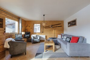 Un salon chaleureux avec un canapé gris, un fauteuil gris, une table basse en bois et un téléviseur posé sur un meuble en bois.