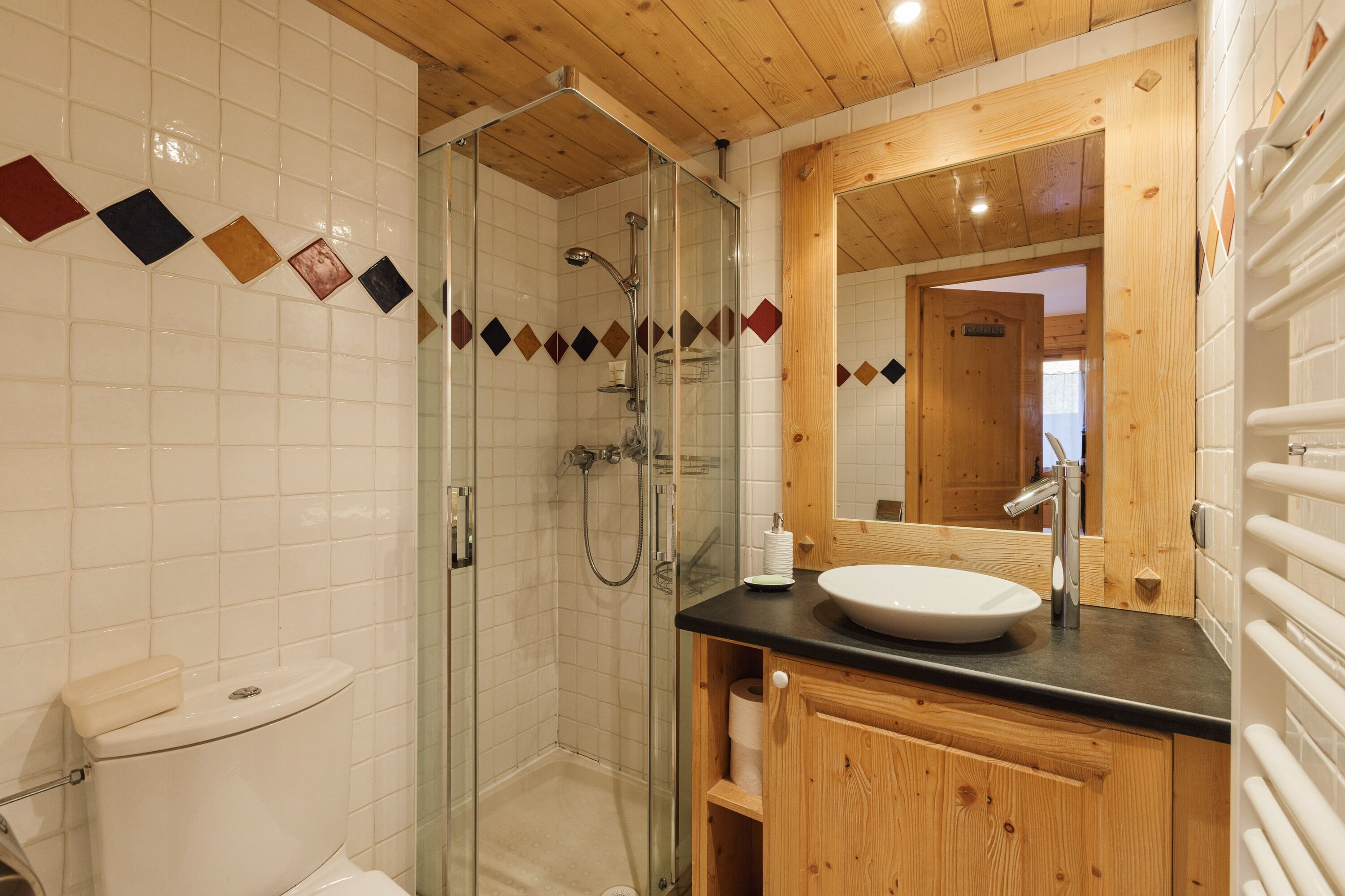 Un bagno con box doccia in vetro, mobile lavabo in legno e lavandino bianco.