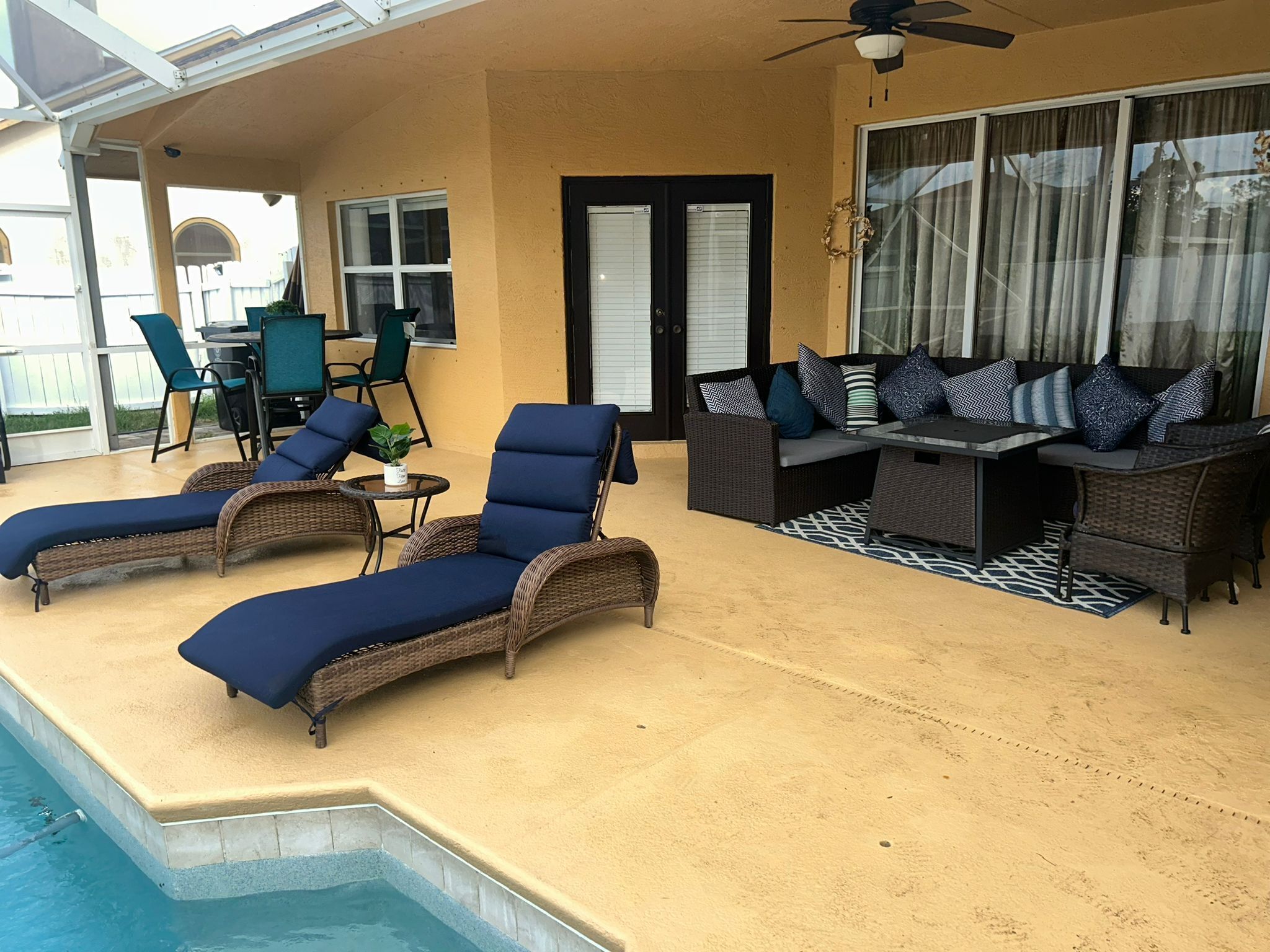 A covered outdoor area with a pool, lounge chairs, a table, and a sofa.
