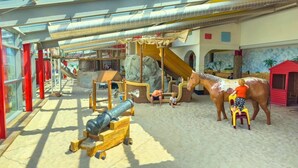 Un área de juegos interior con toboganes, estructuras para escalar y una gran estatua de un caballo.