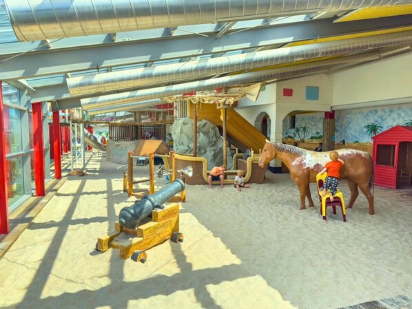 An indoor play area with slides, climbing structures, and a large horse statue.