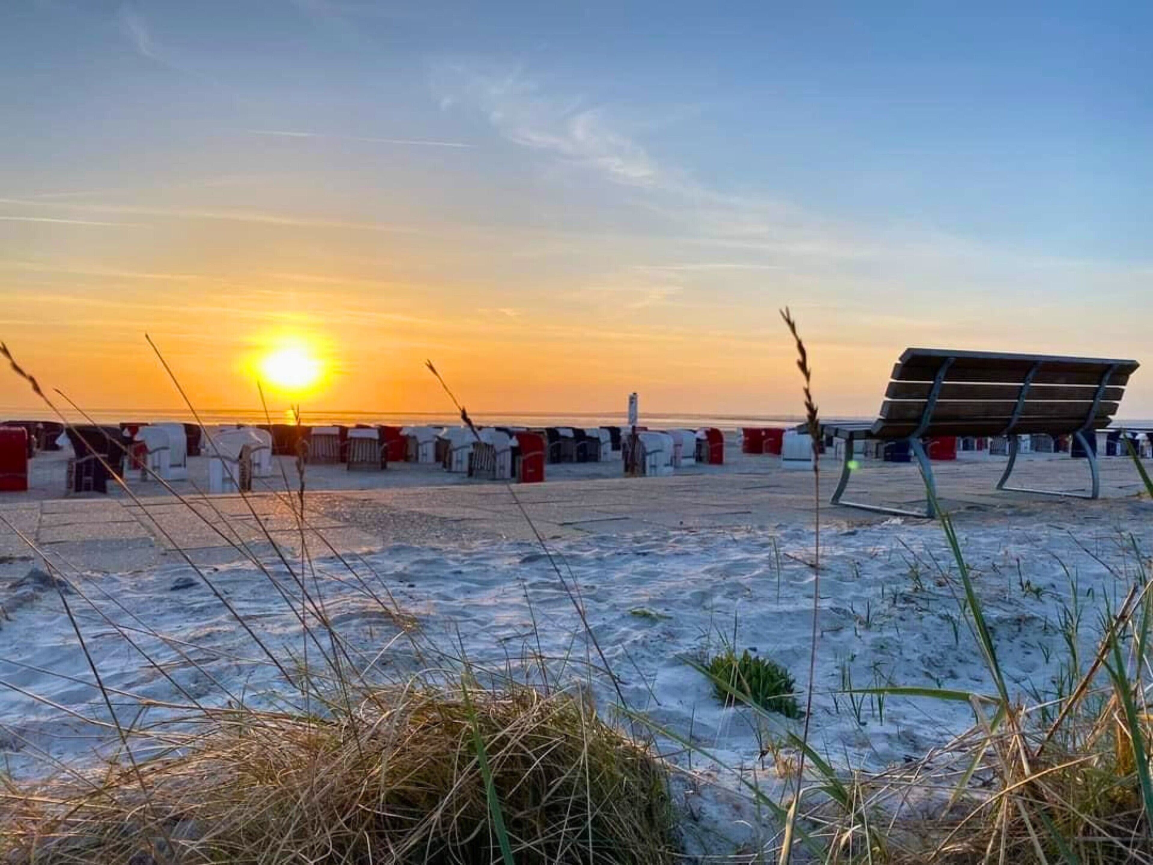 Ein Strand mit einer Bank, Zelten und einem Sonnenuntergang.