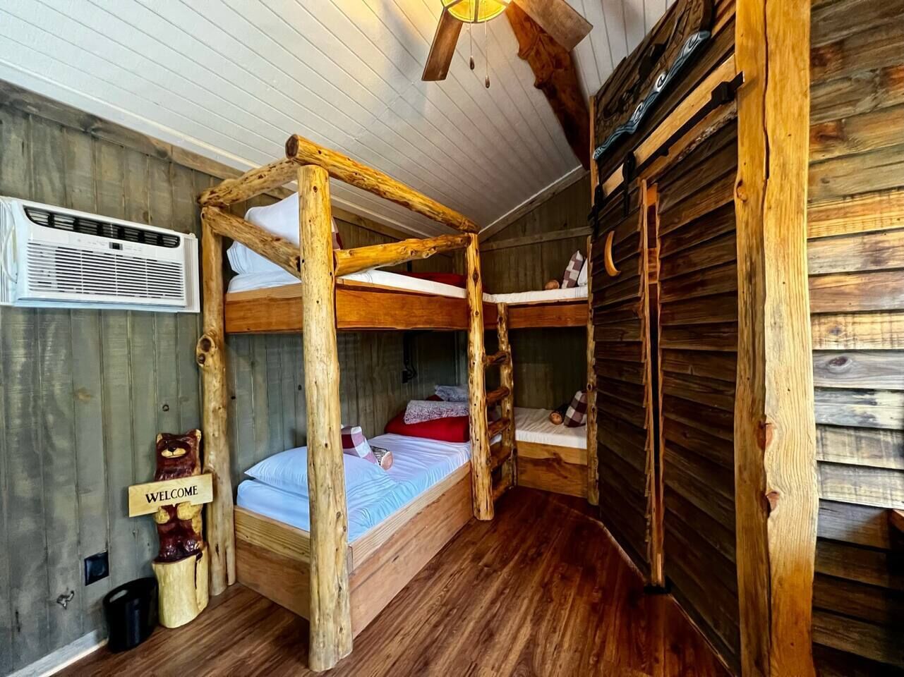 A rustic room with a wooden bunk bed, a welcome sign, and a ladder.