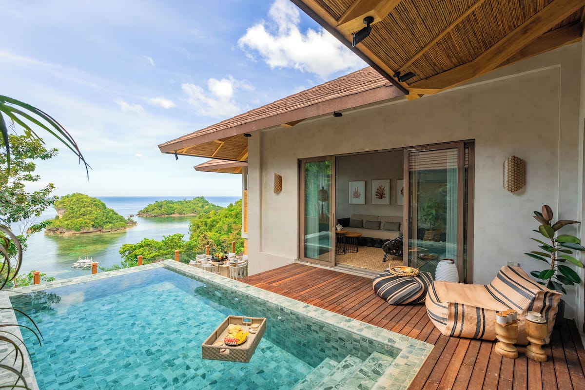 Un espace aménagé au bord de la piscine, avec vue sur la mer, une terrasse en bois et un coin salon avec des coussins.