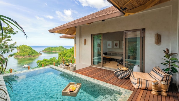 A poolside area with a view of the sea, wooden deck, and a seating area with cushions. - Manami Resort (Sipalay)