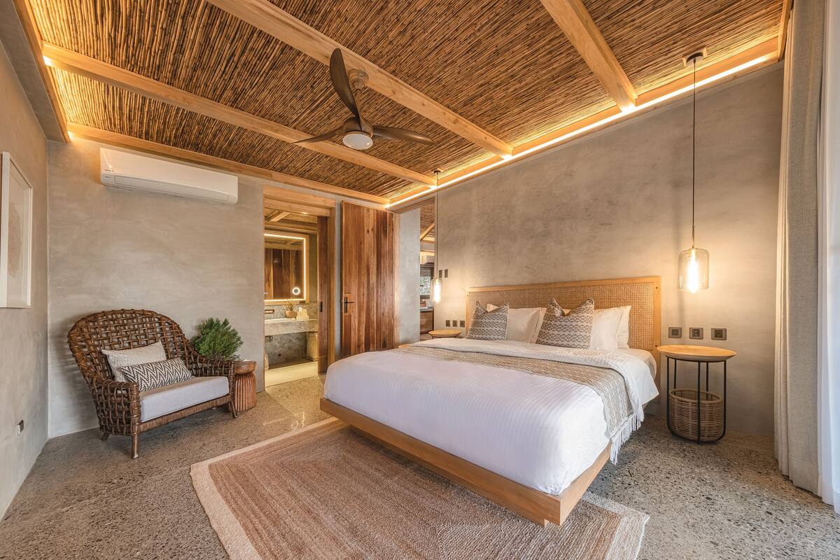 Une chambre moderne avec un grand lit, un fauteuil en osier et un ventilateur de plafond.