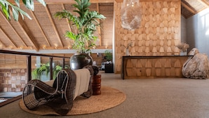 A modern interior with a high ceiling, wooden beams, a woven chair, a large plant, and a reception desk. - Manami Resort (Sipalay)