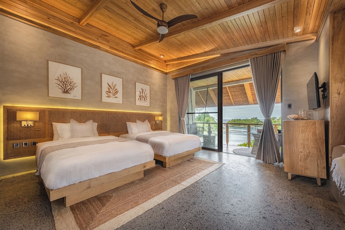 Une chambre d’hôtel avec deux lits, un ventilateur de plafond, une grande fenêtre avec des rideaux et une vue sur l’extérieur.