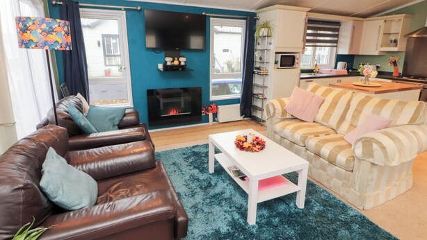 A living room with a brown leather sofa, a striped sofa, a white coffee table, and a fireplace. - Rosie's Zen Den (Carlisle)