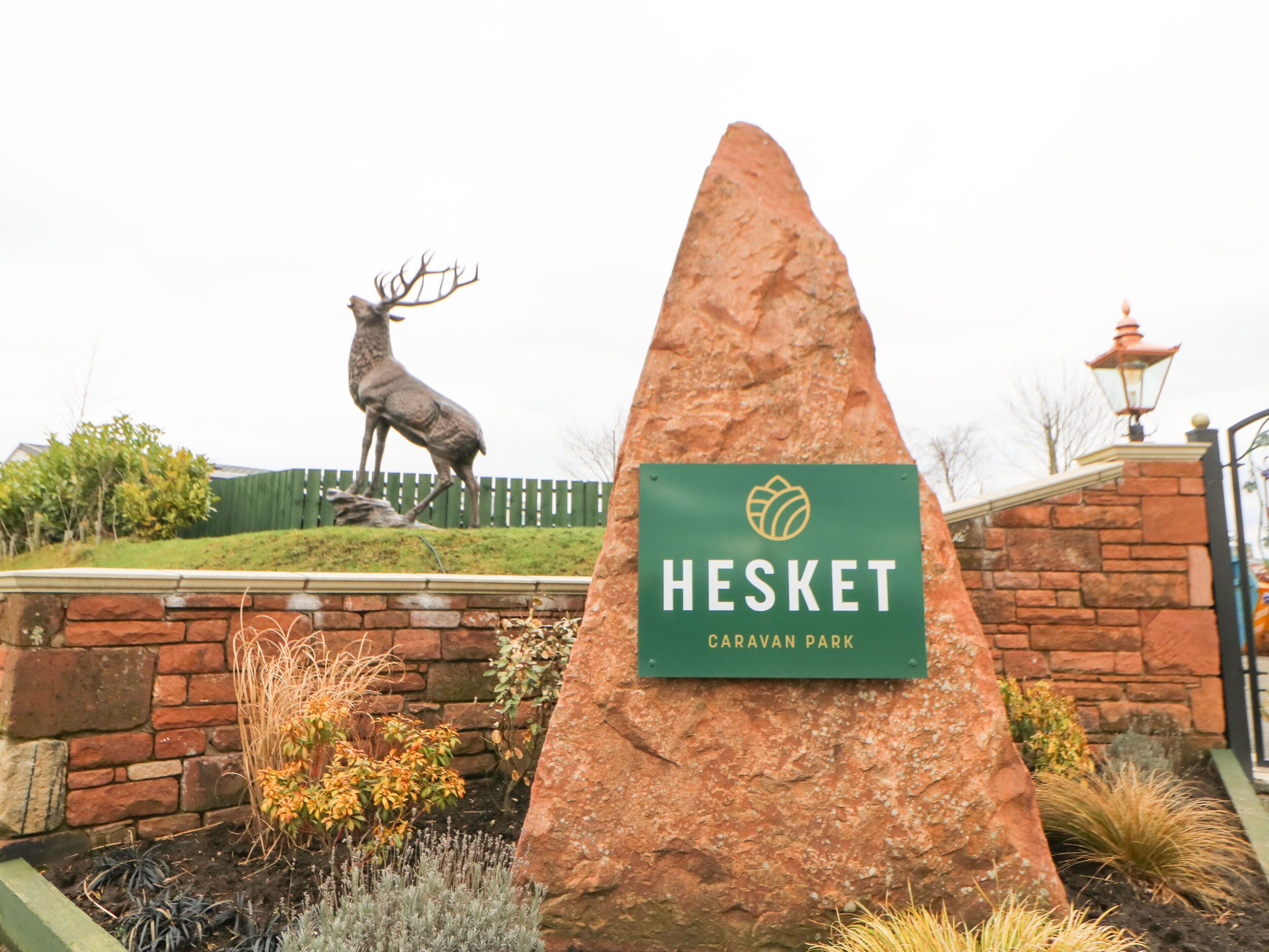 Schild für den Hesket Caravan Park, im Hintergrund eine Hirschstatue.