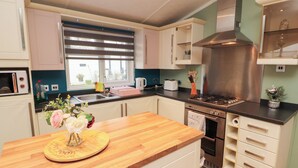 A modern kitchen with white cabinets, a wooden countertop, a stainless steel range hood, and a window with blinds. - Rosie's Zen Den (Carlisle)