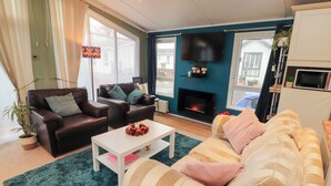A living room with a fireplace, two sofas, a coffee table, and a television. - Rosie's Zen Den (Carlisle)