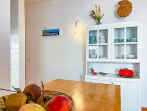 Ein Essbereich mit einem Holztisch, einem Obstkorb, einer weißen Vitrine mit Glastüren und einer wandmontierten Leuchte.