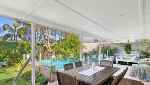 A covered outdoor area with a pool, wooden furniture, and lush greenery.