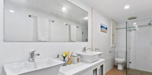 Een moderne badkamer met twee wastafels, een grote spiegel, een toilet en een douchecabine met glazen wanden.