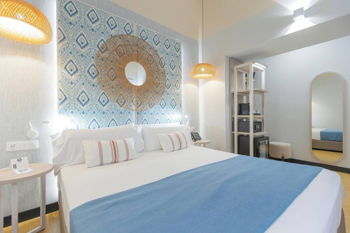 Ein Hotelzimmer mit einem großen Bett, einem Nachttisch, einer Lampe, einem Kleiderschrank und einem Spiegel.