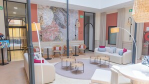 Un moderno vestíbulo de hotel con un área de descanso central, una recepción y un gran mural decorativo.