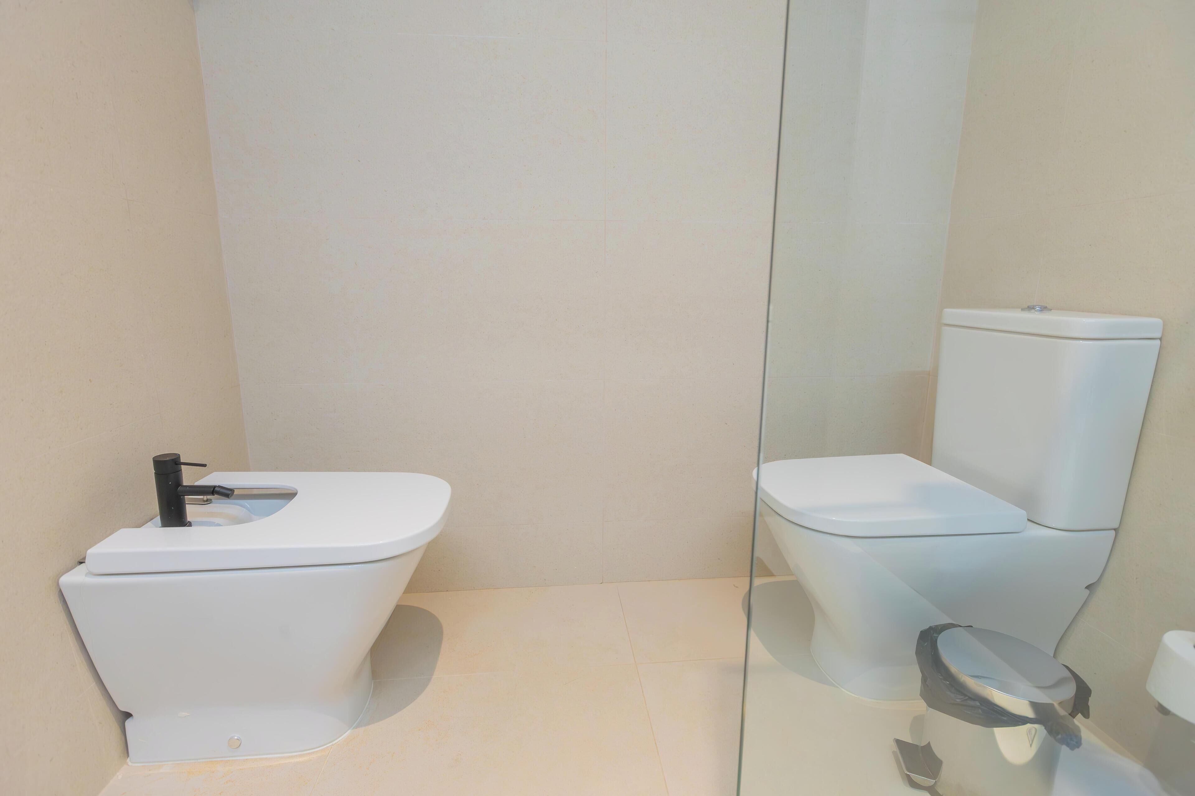 Un baño moderno con inodoro blanco, mampara de vidrio y lavamanos blanco.