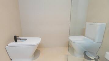 Un baño moderno con inodoro blanco, mampara de vidrio y lavamanos blanco.