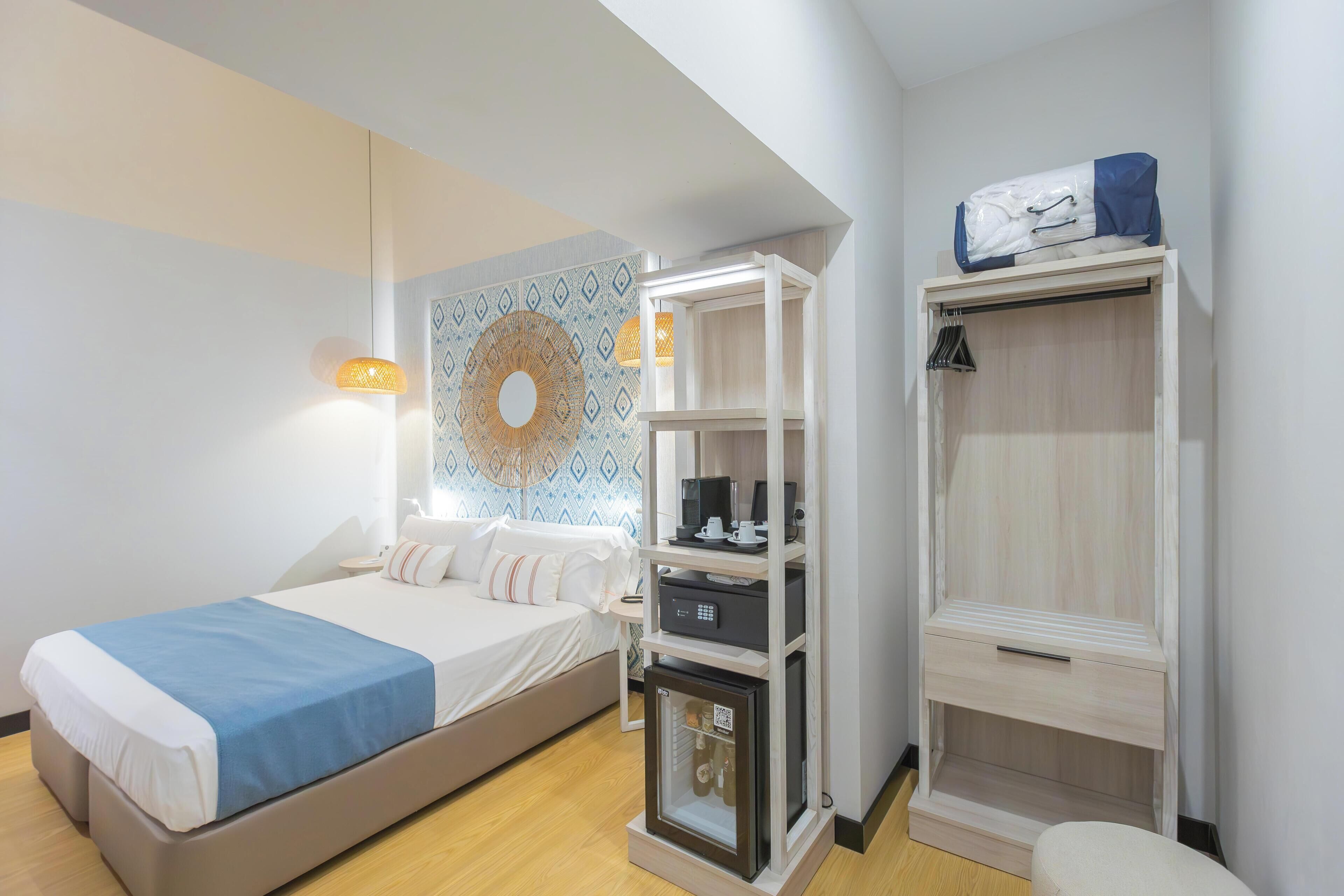 Ein Hotelzimmer mit einem Bett, einem Kleiderschrank, einer kleinen Kommode und einer Wand mit dekorativem Muster.