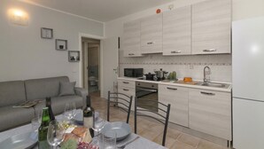 A modern kitchen with light wood cabinets, a dining area with a table set for two, and a grey sofa in the living area. - Porto Letizia Torino 2B, Porlezza, Italy (Porlezza)