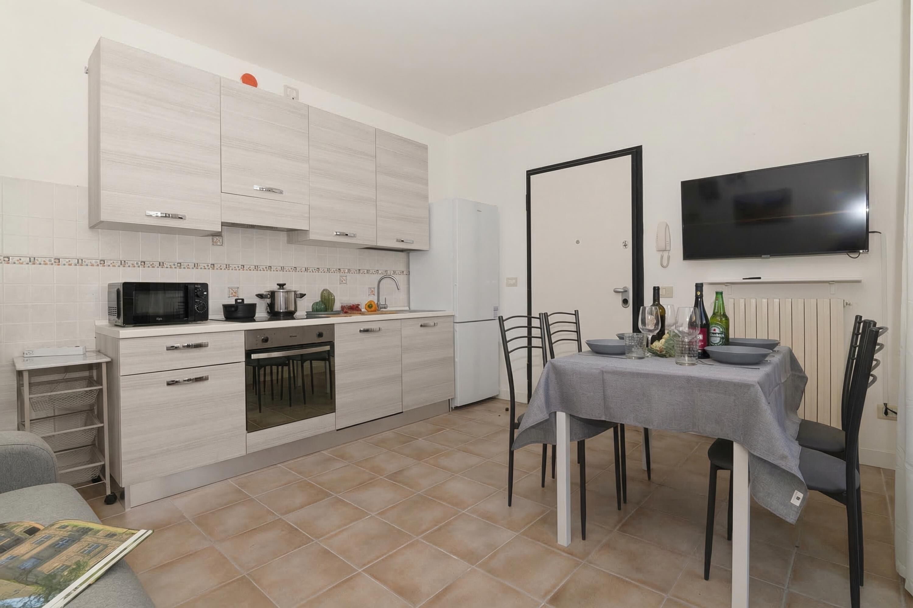Une cuisine compacte dotée d’appareils électroménagers modernes, un coin repas avec une table préparée pour deux personnes, et un téléviseur à écran plat fixé au mur.