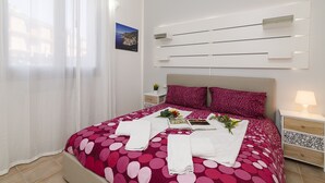 A neatly made bed with a red and pink polka dot bedspread, white towels, and a small bouquet of flowers. - Porto Letizia Torino 2B, Porlezza, Italy (Porlezza)