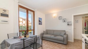 A dining area with a table set for four, a grey sofa, and a kitchen area with a white cabinet. - Porto Letizia Torino 2B, Porlezza, Italy (Porlezza)