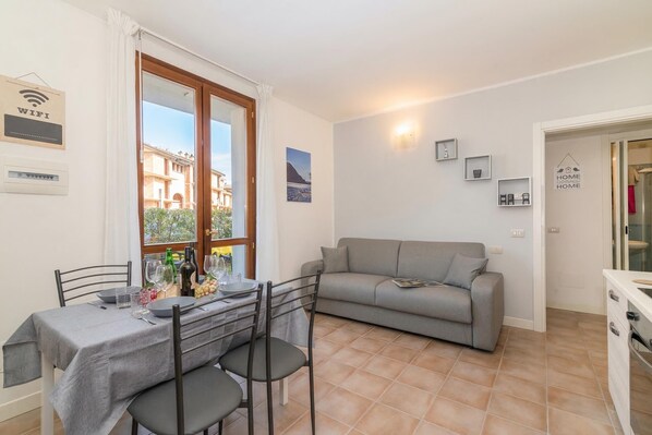 A dining area with a table set for four, a grey sofa, and a kitchen area with a white cabinet.