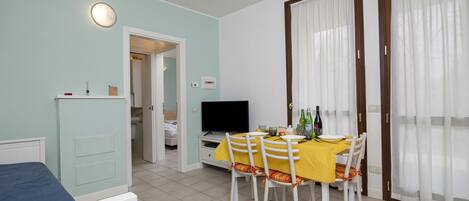 A room with a bed, a dining table with chairs, a TV, and a door leading to another room.