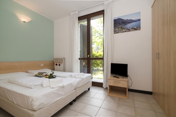 A bedroom with a bed, a TV, a window with curtains, a painting, and a wooden wardrobe. - Porto Letizia Torino 2A, Porlezza, Italy (Porlezza)