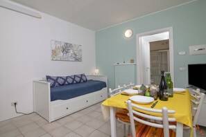 A compact room with a bed, a dining table with chairs, a wall-mounted TV, and a door leading to another room.